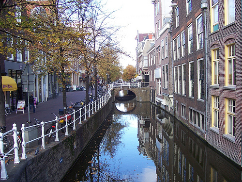 A quiet tree-lined canal in Delft with a small arched bridge